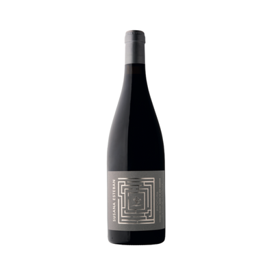 Bottle of Susana Esteban Procura Tinto 2019 on a dark wood table with mountain herbs and black fruits in the background, evoking the wine's powerful structure and origin from old vines in Serra de São Mamede.